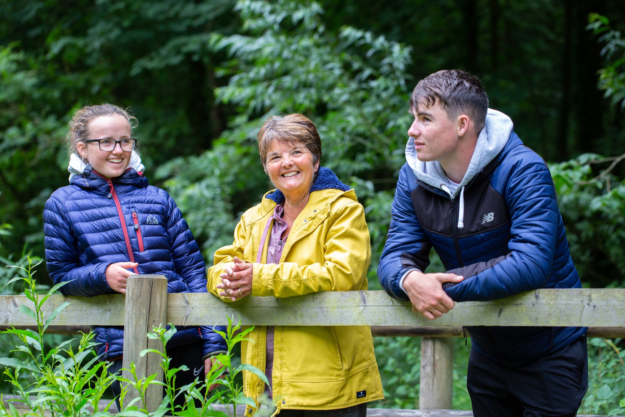 carer and two kids smiling leaning on a fence